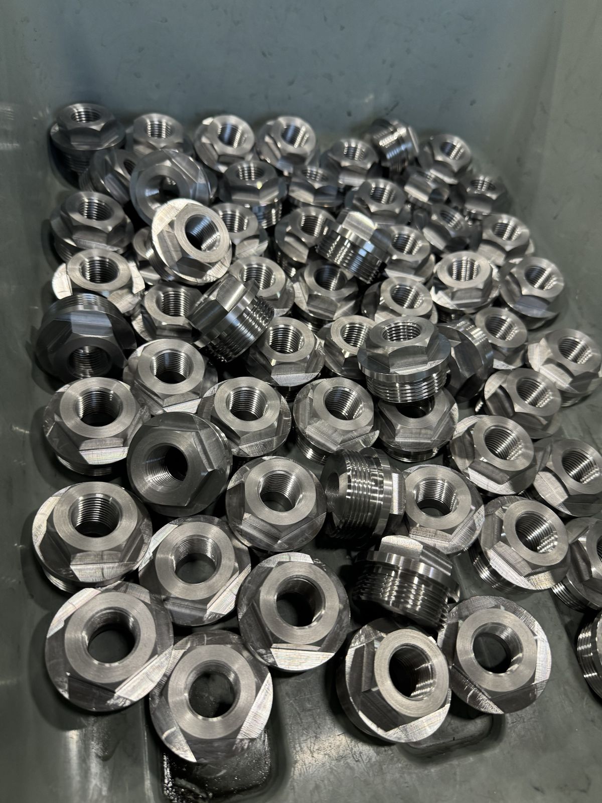 A bin of machined steel hydraulic fittings